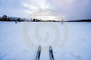 Cross country skiing and ski tip and tracks towards mountain scenery with pink skies. Copy space for own text