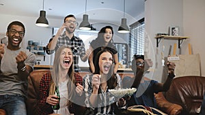 Cross-cultural group watch sports game on TV. Passionate supporters celebrate goal with drinks. 4K slow motion close up.