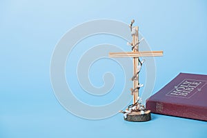 Cross decorated flowers with Holy Bible on blue background. Easter holiday minimalistic concept. Copy space