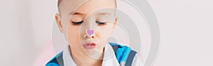 Cross-eyed kid looking at purple violet heart sticker on his nose. Funny hilarious white Caucasian cute adorable child boy making