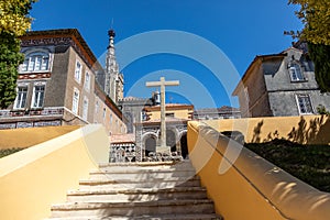 Cross in front of several remaining buildings of Carmelite monastery on background of Bussaco Palace tower in Luso