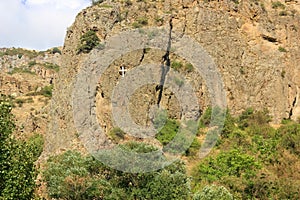 The Cross on an impregnable cliff in mountains opposite the entrance of the rock-cut Medieval Geghard Monastery complex.