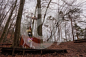 The cross of Jesus Christ in the woods with a garden and flowers around, fall leaves falling around, Slovakia