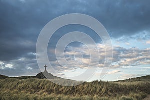 Cross in landscape of Ynys Llanddwyn Island at sunset with moody photo