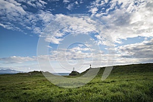 Cross in landscape of Ynys Llanddwyn Island with Twr Mawr lighthouse in background with blue sky photo