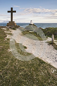 Cross in landscape of Ynys Llanddwyn Island with Twr Mawr lighthouse in background with blue sky