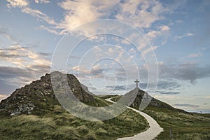 Cross in landscape of Ynys Llanddwyn Island with Twr Mawr lighthouse in background with blue sky