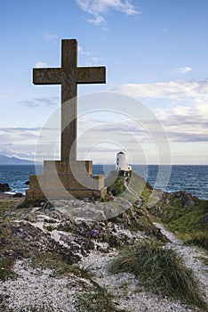 Cross in landscape of Ynys Llanddwyn Island with Twr Mawr lighthouse in background with blue sky