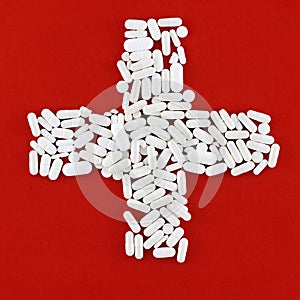 Cross made of white pills (red background)