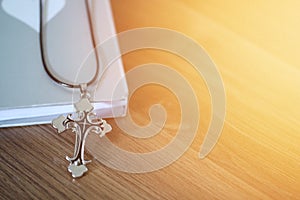 Cross pendant over the book on wooden floor with light flare and copy space