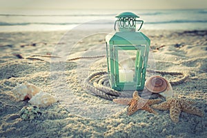 Cross-processed lantern on beach with shells and rope at sunrise photo