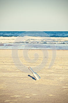 Cross processed photo of a bottle with letter on beach, shallow