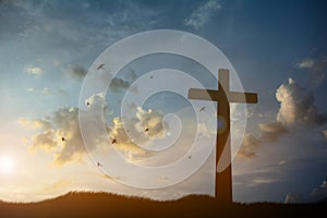 Cross religion symbol silhouette in grass over sunset or sunrise sky