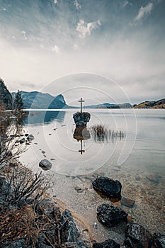 Cross on rock in lake Mond surrounded mountains