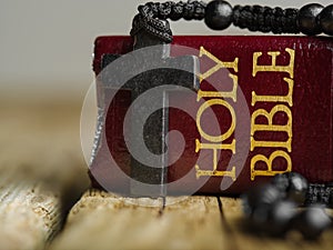 Cross and rosary against the background of the holy bible on a wooden table in the church