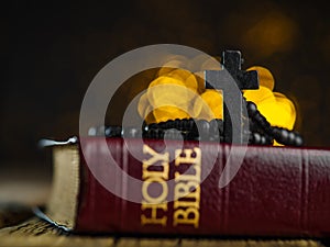 A cross and a rosary against the background of a holy bible on a wooden table in a church with lights from the light.The concept