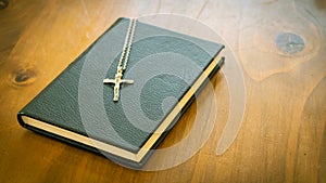 The Cross with the Rosary in the Holy Bible The book is closed, closed with a black cover and Christian symbol on a wooden