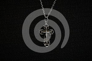 Cross on a silver chain, faith, spirituality and religion, dark fabric background.