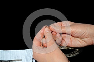 Cross-stitch. Needle for embroidery in female hands. White fabric with a pattern. The pattern is brown, black and beige.