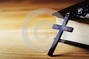 Cross on a thread with black beads with a bible on a wooden table. Religious symbol, prayer. Copy space.