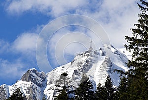 Cross on the top of a rocky mountain covered in the snow under a blue cloudy sky