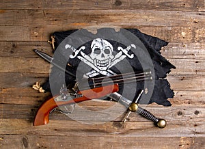 Crossed antique flintlock pistol large pirate dagger and jolly roger flag on a rough wooden table