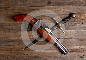 Crossed antique flintlock pistol and large pirate dagger on a rough wooden table