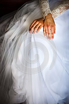 Crossed feamle hands are laying on the white wedding dress closeup photo