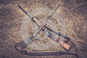 Crossed hunting shotguns with ammunition belt in retro vintage style on dry grass as hunting background