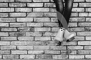 Crossed legs of a young girl in jeans and orange galoshes sitting on a brick wall against a brick wall background