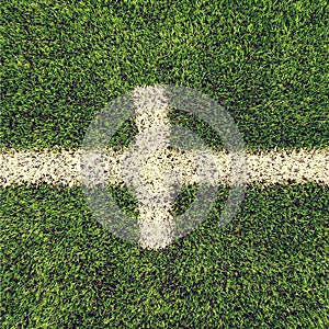 Crossed white lines on outdoor football playground. Detail of lines in a soccer field. Plastic grass and finely ground b