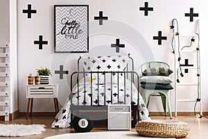 Crosses on white wall and bedding in stylish bedroom interior with industrial metal bed and modern mint grey chair