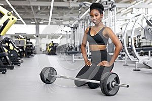 Crossfit african woman sitting at gym, resting after cross-fit workout with barbell