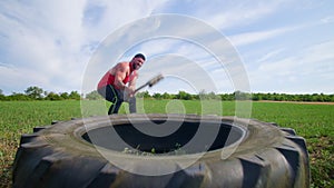 Crossfit Athlete Muscular Man Demonstrating Tire Hitting Exercise with Sledgehammer, slowmo