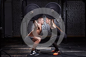 Crossfit lifting bar by woman and man in group workout against brick wall.