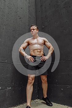 Strong and muscular bodybuilder showing his body near concrete wall