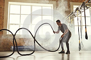 CrossFit training. Side view of young athletic man with perfect body doing crossfit exercises with a rope in the gym.