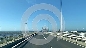 Crossing the bridge to wind turbine and solar farm. Renewable energy. Sunny day with blue sky.