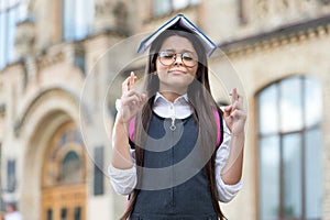 Crossing fingers for luck. Little geek make wish outdoors. Small child hold book on head. Knowledge day. September 1