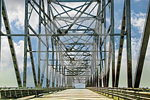 Crossing a multi-span highway truss bridge over river with cloudy blue sky