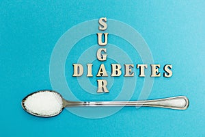 Crossing the words `sugar` and `diabetes`, a spoon with sugar on a blue background, concept.