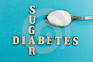 Crossing the words `sugar` and `diabetes`, a spoon with sugar on a blue background, concept