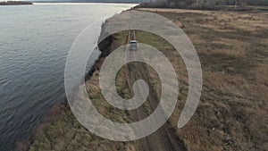 Crossover car riding on sea shore along autumn field aerial view. Tourist off road suv car driving along countryside field on sea