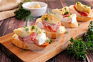 Crostini appetizers with brie cheese, salami and artichokes, close up on a serving board against a wood background photo