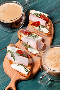 Crostini appetizers with figs, brie cheese arugula and sun-dried tomatoes, ham. Close up on a slate serving board against over