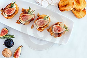 Crostini appetizers with figs, brie cheese and nuts, overhead view on plate with a marble background