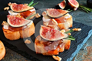 Crostini appetizers with figs, brie cheese and nuts, close up against dark slate