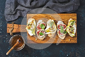 Crostini with fruits, cheese and herbs on rustic wooden board