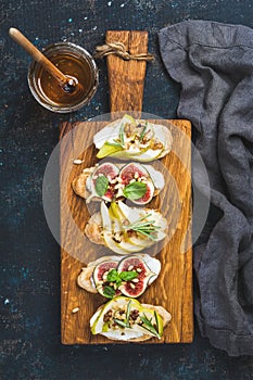 Crostini with fruits, cheese and herbs on rustic wooden board