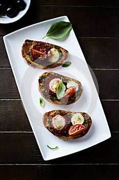 Crostini with tomato, salami and olive pesto on wooden background.